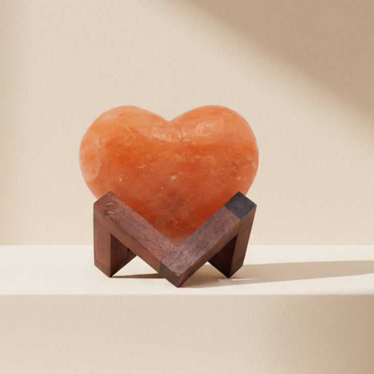 Heart-shaped orange salt lamp on a wooden stand against a white background